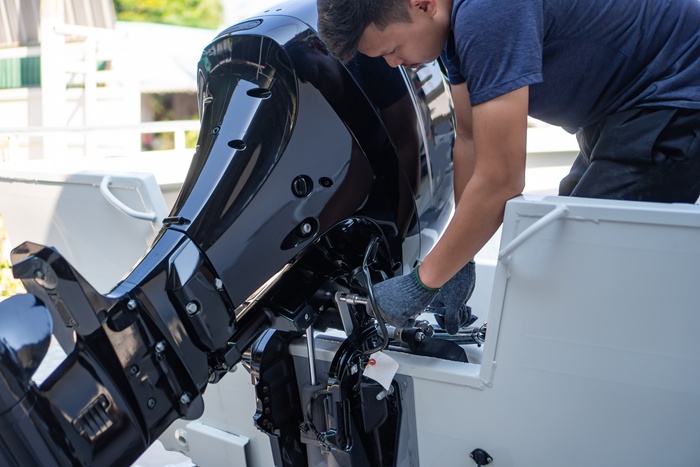A boat engine that appears brand new and shiny. A man wearing gloves is working on a part of the engine.