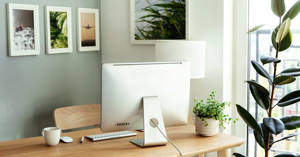 A desk in a home office with an Apple computer on it. Several framed photos of plants and planes are hanging on the wall.