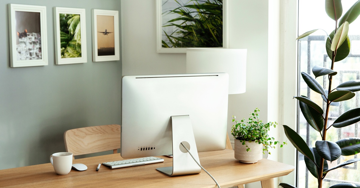 A desk in a home office with an Apple computer on it. Several framed photos of plants and planes are hanging on the wall.