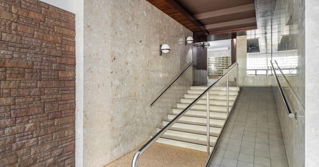 A corridor of a building has a small set of steps alongside a ramp. The walls of the corridor are stone and granite.