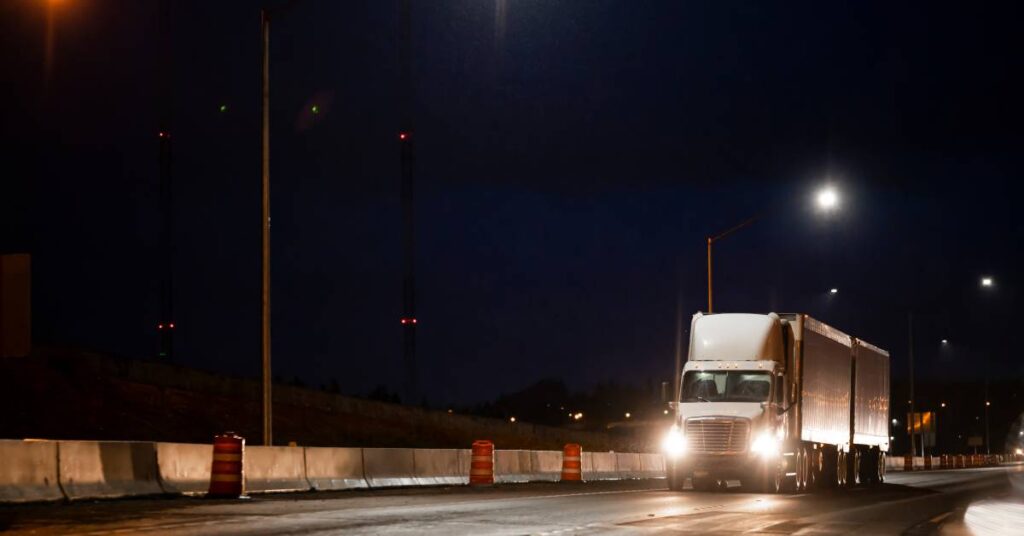 A large white semi-truck cab is hauling cargo in two trailers on a wet highway after a rainstorm at night.