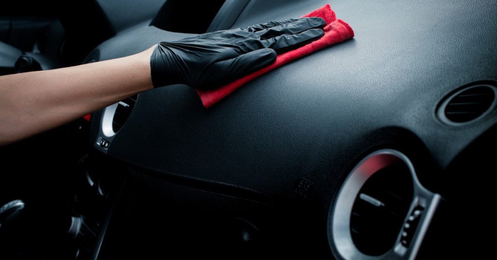 A close-up view shows a hand wearing a black latex glove pressing a red rag onto a vehicle's black interior.