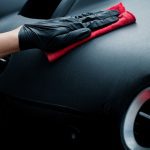 A close-up view shows a hand wearing a black latex glove pressing a red rag onto a vehicle's black interior.