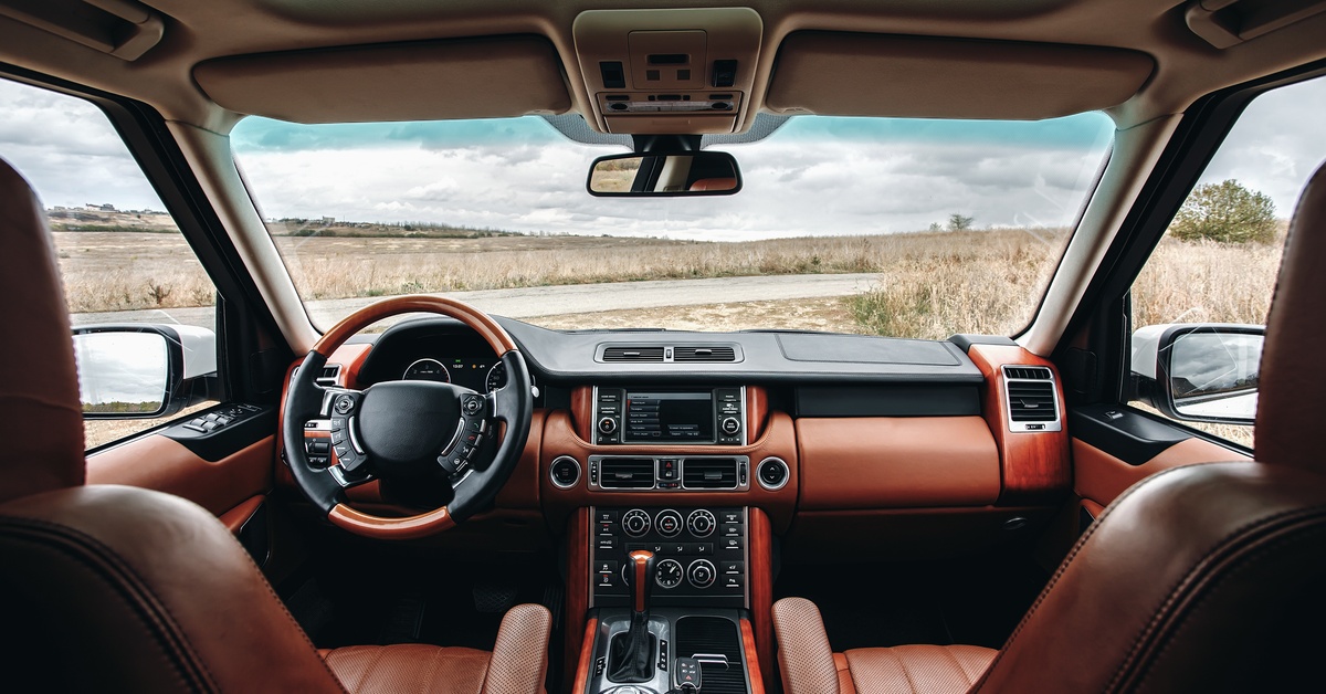 The interior of a new car, looking out on an empty road. The car is modern with brown and black upholstery.