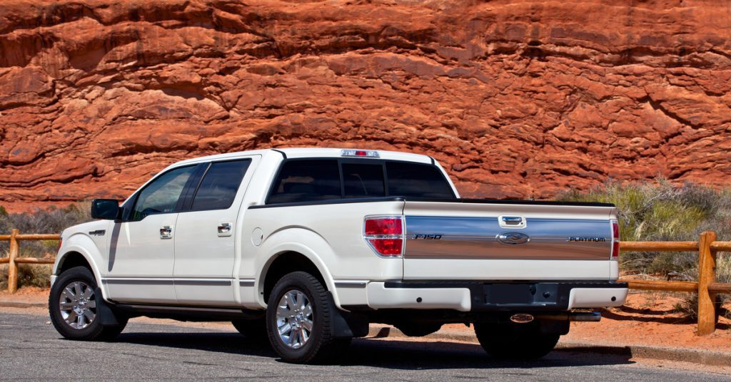 A white pickup truck with an extended cab is parked next to a wooden fence. Red rocks appear in the background.