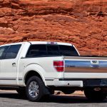 A white pickup truck with an extended cab is parked next to a wooden fence. Red rocks appear in the background.
