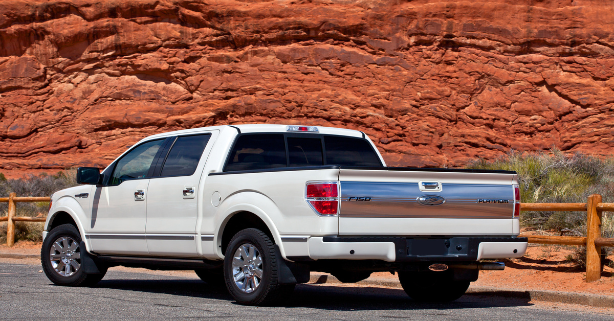 A white pickup truck with an extended cab is parked next to a wooden fence. Red rocks appear in the background.