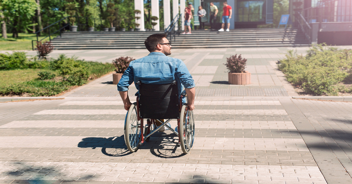 A man in a wheelchair is going across a crosswalk in a city. He is looking to his side as he moves toward the sidewalk.