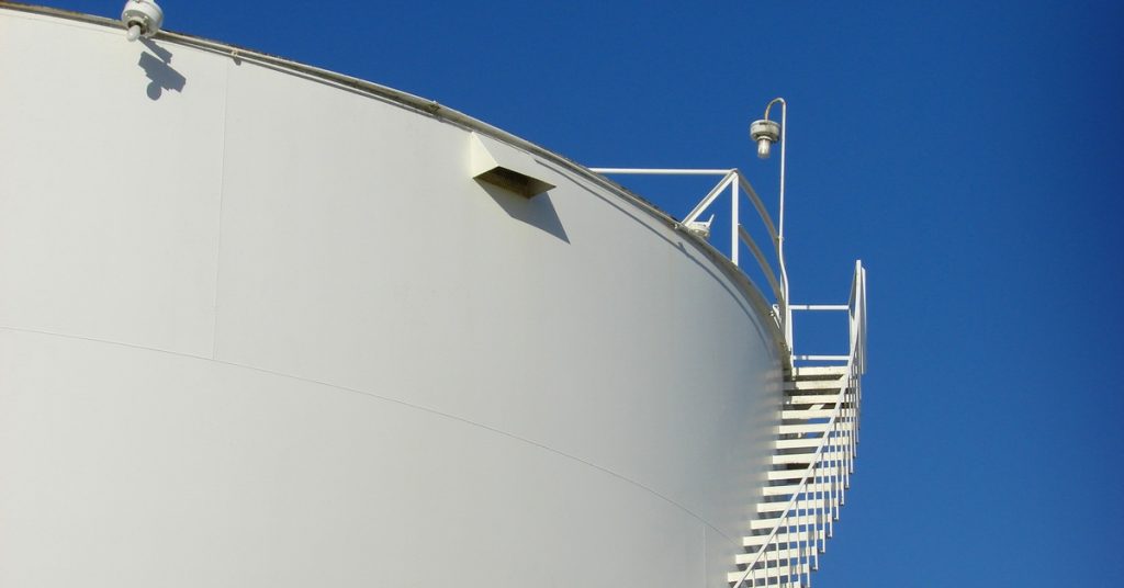 A close-up view shows a white industrial tank with a white staircase and a white light post on top.