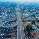 An aerial view of a crowded city with new urban landscaping and a winding road in the middle of the city.