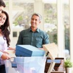 Parents helping their teenage son pack for college; both parents smile at their son as he packs his boxes.