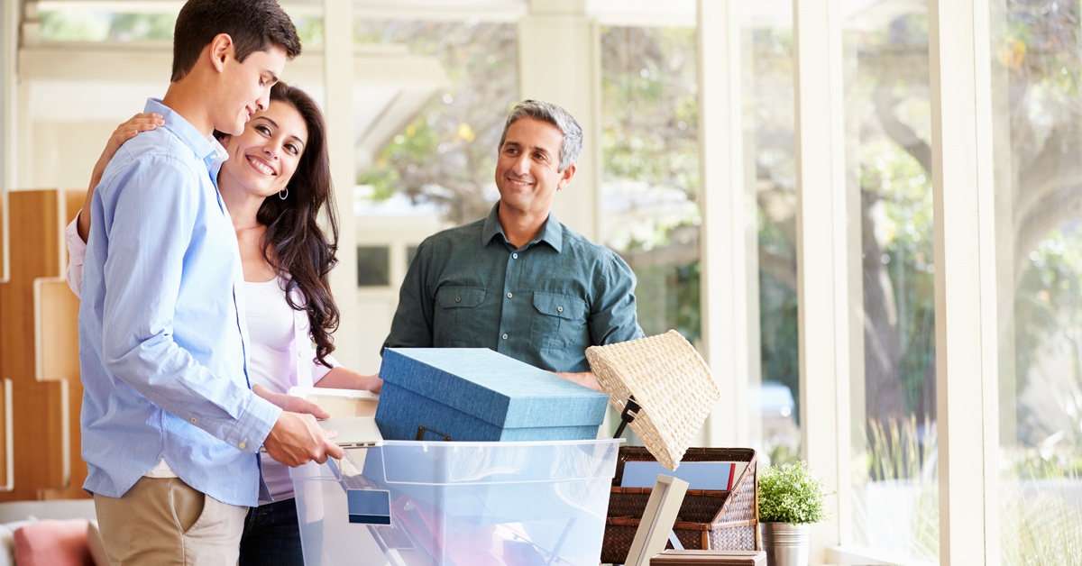 Parents helping their teenage son pack for college; both parents smile at their son as he packs his boxes.