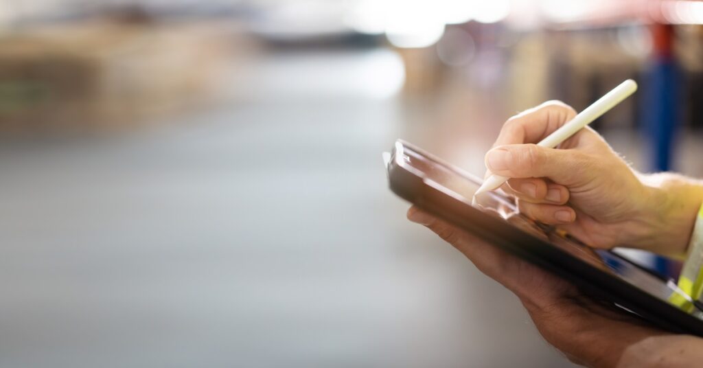 A close-up of a professional warehouse staff member using a digital tablet to review the stock inventory on the shelf.